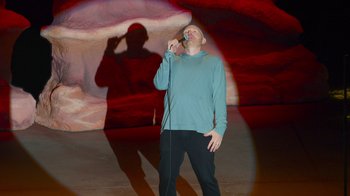 Movie still from “Bill Burr: Live at Red Rocks” (2022), directed by Mike Binder – A man standing in front of a microphone on a stage; Wide shot, High angle