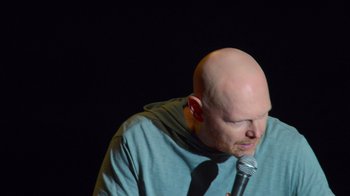 Movie still from “Bill Burr: Live at Red Rocks” (2022), directed by Mike Binder – A bald man with a microphone in front of a black background; Close Up shot, High angle