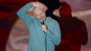 Movie still from “Bill Burr: Live at Red Rocks” (2022), directed by Mike Binder – A bald man holding a microphone up to his head; Medium shot, High angle