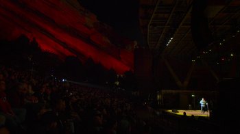 Movie still from “Bill Burr: Live at Red Rocks” (2022), directed by Mike Binder – A crowd of people sitting in front of stage lights; Extreme Wide shot, High angle