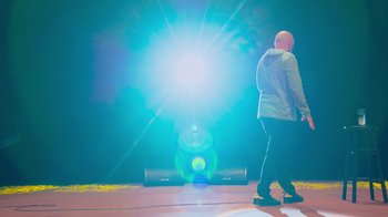 Movie still from “Bill Burr: Live at Red Rocks” (2022), directed by Mike Binder – A man standing in front of a speaker on a stage; Wide shot, Low angle
