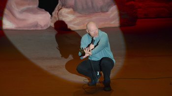 Movie still from “Bill Burr: Live at Red Rocks” (2022), directed by Mike Binder – A man in a blue shirt is holding a microphone; Wide shot, High angle