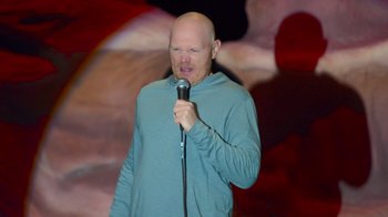 Movie still from “Bill Burr: Live at Red Rocks” (2022), directed by Mike Binder – A bald man in a blue shirt is holding a microphone; Medium shot, High angle
