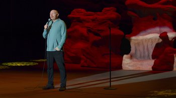 Movie still from “Bill Burr: Live at Red Rocks” (2022), directed by Mike Binder – A man standing on a stage holding a microphone; Wide shot, High angle
