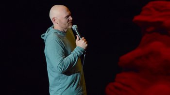 Movie still from “Bill Burr: Live at Red Rocks” (2022), directed by Mike Binder – A bald man holding a microphone while standing on a stage; Medium shot, Over the shoulder angle