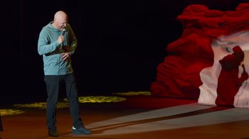 Movie still from “Bill Burr: Live at Red Rocks” (2022), directed by Mike Binder – A man standing on a stage holding a microphone; Wide shot, High angle