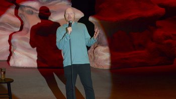 Movie still from “Bill Burr: Live at Red Rocks” (2022), directed by Mike Binder – A man standing on a stage holding a microphone; Wide shot, High angle