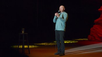 Movie still from “Bill Burr: Live at Red Rocks” (2022), directed by Mike Binder – A man standing on a stage holding a microphone; Medium shot, High angle