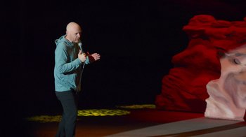 Movie still from “Bill Burr: Live at Red Rocks” (2022), directed by Mike Binder – A bald man standing on a stage holding a microphone; Wide shot, Low angle