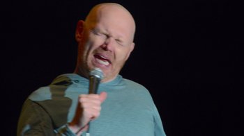 Movie still from “Bill Burr: Live at Red Rocks” (2022), directed by Mike Binder – A bald man is holding a microphone up to his face; Close Up shot, High angle