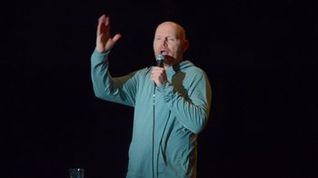 Movie still from “Bill Burr: Live at Red Rocks” (2022), directed by Mike Binder – A bald man is holding a microphone up to his mouth; Medium shot, Low angle