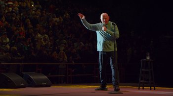 Movie still from “Bill Burr: Live at Red Rocks” (2022), directed by Mike Binder – A man standing on a stage holding a microphone; Medium shot, High angle