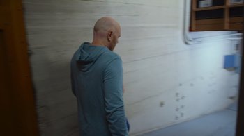 Movie still from “Bill Burr: Live at Red Rocks” (2022), directed by Mike Binder – A bald man in a blue shirt is standing in front of a white wall; Medium shot, Low angle