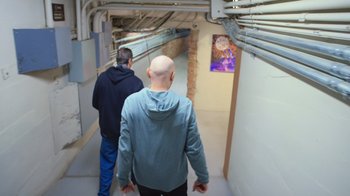 Movie still from “Bill Burr: Live at Red Rocks” (2022), directed by Mike Binder – Two men are walking down the hallway of a building; Wide shot, Over the shoulder angle