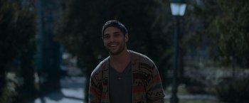 Movie still from “Birds of Paradise” (2021), directed by Sarah Adina Smith – A young man smiling while standing in the dark; Medium shot, High angle