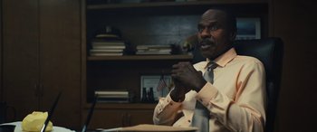 Movie still from “Birds of Prey” (2020), directed by Cathy Yan – A man sitting at a desk in front of an american flag; Medium shot, Low angle