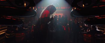 Movie still from “Birds of Prey” (2020), directed by Cathy Yan – A woman is singing into a microphone in a dark room; Wide shot, Over the shoulder angle