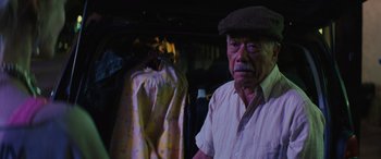 An older man wearing a hat standing in front of clothes