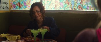 Movie still from “Birds of Prey” (2020), directed by Cathy Yan – A woman sitting at a table with two glasses of green liquid; Medium shot, Over the shoulder angle