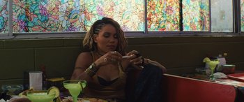 Movie still from “Birds of Prey” (2020), directed by Cathy Yan – A woman sitting at a table looking at her cell phone; Medium shot, Over the shoulder angle