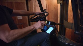 Movie still from “Bitchin': The Sound and Fury of Rick James” (2021), directed by Sacha Jenkins – A person is using a cell phone while sitting on a forklift; Medium shot, Overhead angle