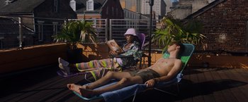 Movie still from “Black as Night” (2021), directed by Maritte Lee Go – A man and a woman sitting on lounge chairs reading; Wide shot, High angle