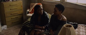 Movie still from “Black as Night” (2021), directed by Maritte Lee Go – Two women sitting on a couch talking to each other; Medium shot, High angle