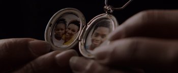 Movie still from “Black as Night” (2021), directed by Maritte Lee Go – A person holding an open locket with a picture of two people; Extreme Close Up shot, Overhead angle