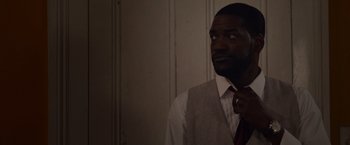 Movie still from “Black as Night” (2021), directed by Maritte Lee Go – A man in a suit and tie looking at the camera; Close Up shot, Low angle