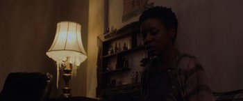 Movie still from “Black as Night” (2021), directed by Maritte Lee Go – A person standing in a room with a lamp in the background; Close Up shot, Low angle