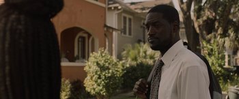 Movie still from “Black as Night” (2021), directed by Maritte Lee Go – A man in a tie standing in front of a house; Close Up shot, Over the shoulder angle