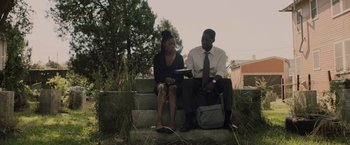 Movie still from “Black as Night” (2021), directed by Maritte Lee Go – A man and a woman sitting on a stone bench; Medium shot, Low angle