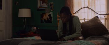 Movie still from “Black as Night” (2021), directed by Maritte Lee Go – A woman is using a laptop on the bed; Medium shot, Low angle