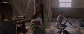 Movie still from “Black as Night” (2021), directed by Maritte Lee Go – A woman holding a stack of papers in her hands; Medium shot, Over the shoulder angle