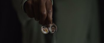 Movie still from “Black as Night” (2021), directed by Maritte Lee Go – A person holding a picture of a child in a locket; Extreme Close Up shot, Overhead angle