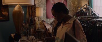 Movie still from “Black as Night” (2021), directed by Maritte Lee Go – A woman sitting at a table looking at her cell phone; Medium shot, Over the shoulder angle