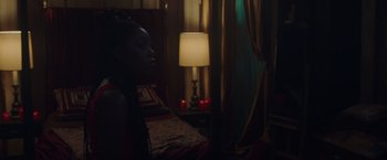 Movie still from “Black as Night” (2021), directed by Maritte Lee Go – A woman sitting on a bed next to a lamp; Medium shot, Over the shoulder angle