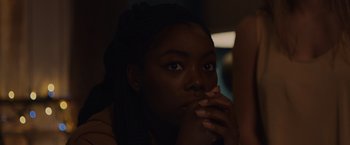 Movie still from “Black as Night” (2021), directed by Maritte Lee Go – A young woman with long black hair is sitting in a dark room; Close Up shot, Over the shoulder angle