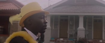 Movie still from “Black as Night” (2021), directed by Maritte Lee Go – A man wearing a yellow hat standing in front of a house; Close Up shot, Low angle