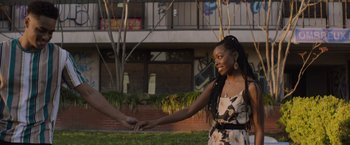 Movie still from “Black as Night” (2021), directed by Maritte Lee Go – A woman holding a man's hand while standing in a park; Medium shot, Over the shoulder angle