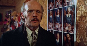 Movie still from “Black Christmas” (1974), directed by Bob Clark – An older man wearing a suit and tie in front of pictures; Close Up shot, Over the shoulder angle