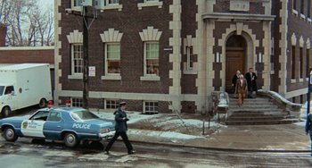 Movie still from “Black Christmas” (1974), directed by Bob Clark – A police officer crossing the street in front of a building; Extreme Wide shot, High angle