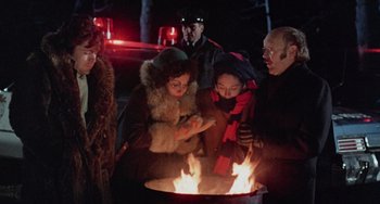 Movie still from “Black Christmas” (1974), directed by Bob Clark – A group of people standing around a fire pit at night; Medium shot, High angle