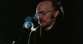 Movie still from “Black Christmas” (1974), directed by Bob Clark – An older man with a beard and glasses smoking a cigarette; Close Up shot, Low angle