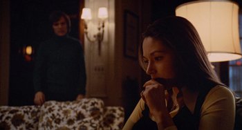 Movie still from “Black Christmas” (1974), directed by Bob Clark – A woman sitting in front of a man in a living room; Medium shot, Over the shoulder angle