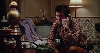 Movie still from “Black Christmas” (1974), directed by Bob Clark – A man talking on a phone while sitting on a table; Medium shot, High angle