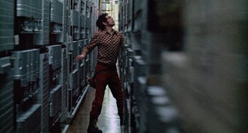 Movie still from “Black Christmas” (1974), directed by Bob Clark – A man is walking in a room with a bunch of cabinets; Wide shot, Low angle