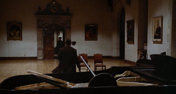 Movie still from “Black Christmas” (1974), directed by Bob Clark – Two men are sitting in a room and one is playing the piano; Extreme Wide shot, High angle