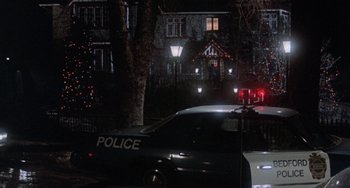 Movie still from “Black Christmas” (1974), directed by Bob Clark – A police car parked in front of a house at night; Extreme Wide shot, Low angle