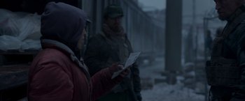 Movie still from “Black Crab” (2022), directed by Adam Berg – Two people standing in the snow looking at papers; Medium shot, Over the shoulder angle